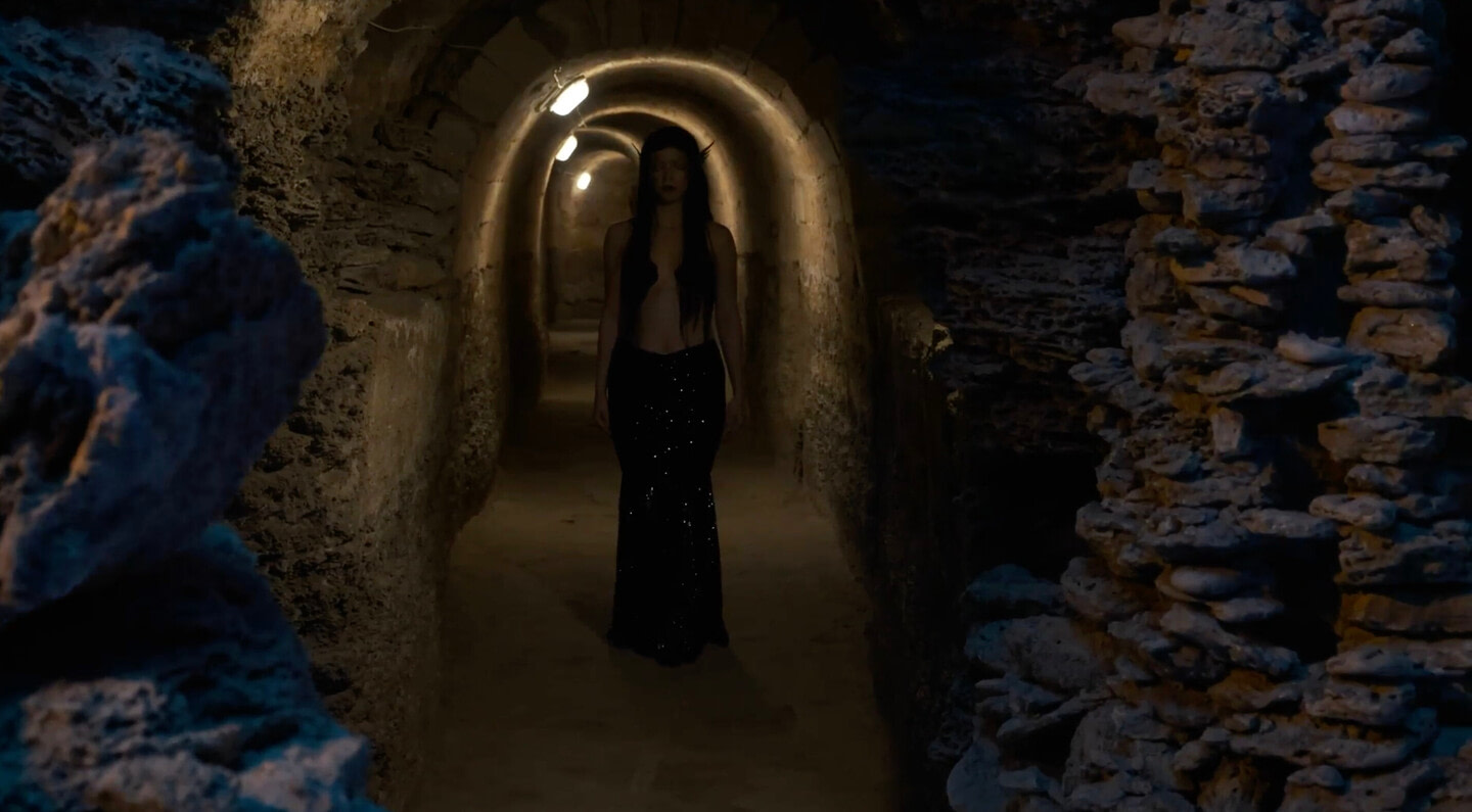 A dark, narrow, arched underground corridor in the Odessa Art Museum, illuminated by a soft, warm light. In the center of the frame is a silhouette of a person walking deeper into the tunnel in performance Sirens